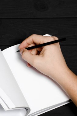 Sapan gibi arka planda bir adamın elinde beyaz bir defter ve siyah bir kalem. Yakın plan.