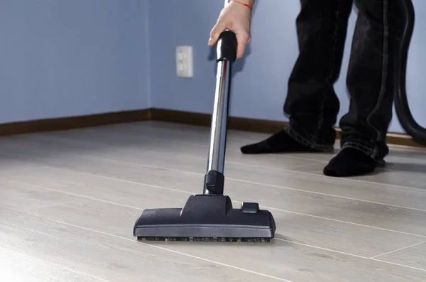 Elinde elektrikli süpürge olan bir adam mavi duvarlı ve ışıklı zemini olan bir odada temizlik yapıyor.