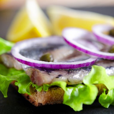 Appetizing sandwich with Norwegian herring, lettuce, blue onion, lemon and tomato lies on a wooden texture board