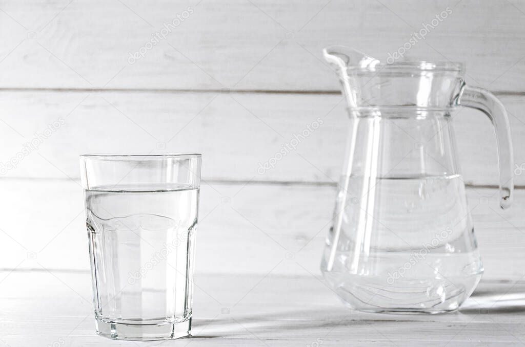 A glass of clean clear water stands on a white wooden background with sharp shadows. shadows