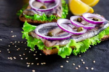 Appetizing sandwich with Norwegian herring, lettuce, blue onion, lemon and tomato lies on a wooden texture board