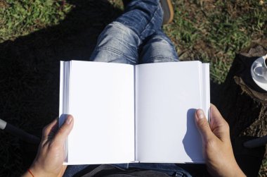 Elinde beyaz bir not defteri olan kot pantolonlu bir adam açık hava koltuğunda oturuyor. Serbest Çalışan