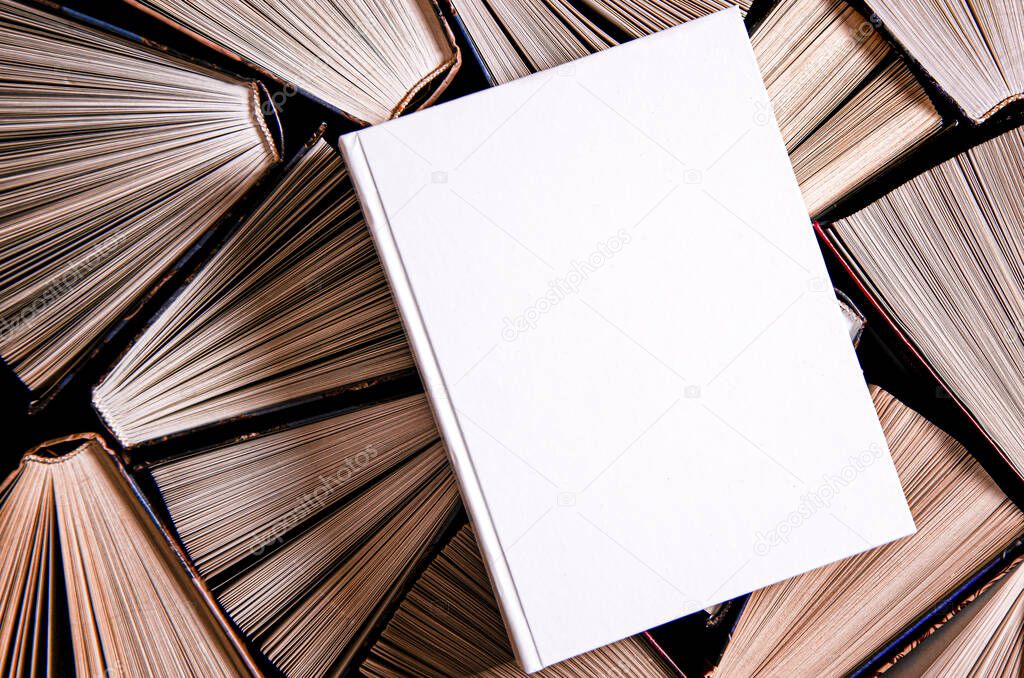 Mockup of closed blank square book at white textured paper background rests on open old multicolored books