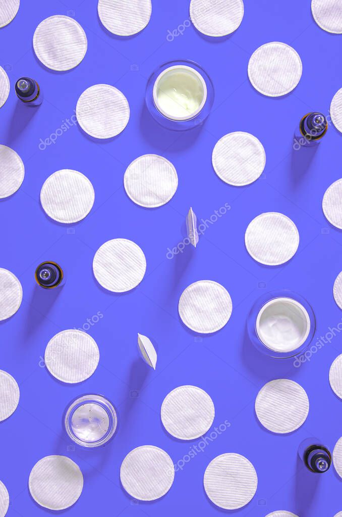 Hygiene products: white round cotton pads and plastic sticks for cleaning the ears lie on a blue background next to face cream. Top view, flat lay