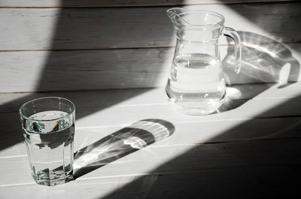 Um copo de água limpa e limpa fica em um fundo de madeira branco com sombras nítidas — Fotografia de Stock