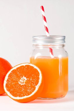 Taze sıkılmış portakal suyuyla dolu cam kavanoz taze portakalların yanında beyaz arka planda duruyor. izole