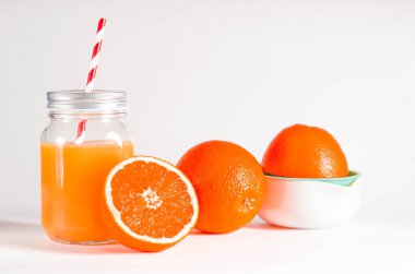 Taze sıkılmış portakal suyuyla dolu cam kavanoz taze portakalların yanında beyaz arka planda duruyor. izole
