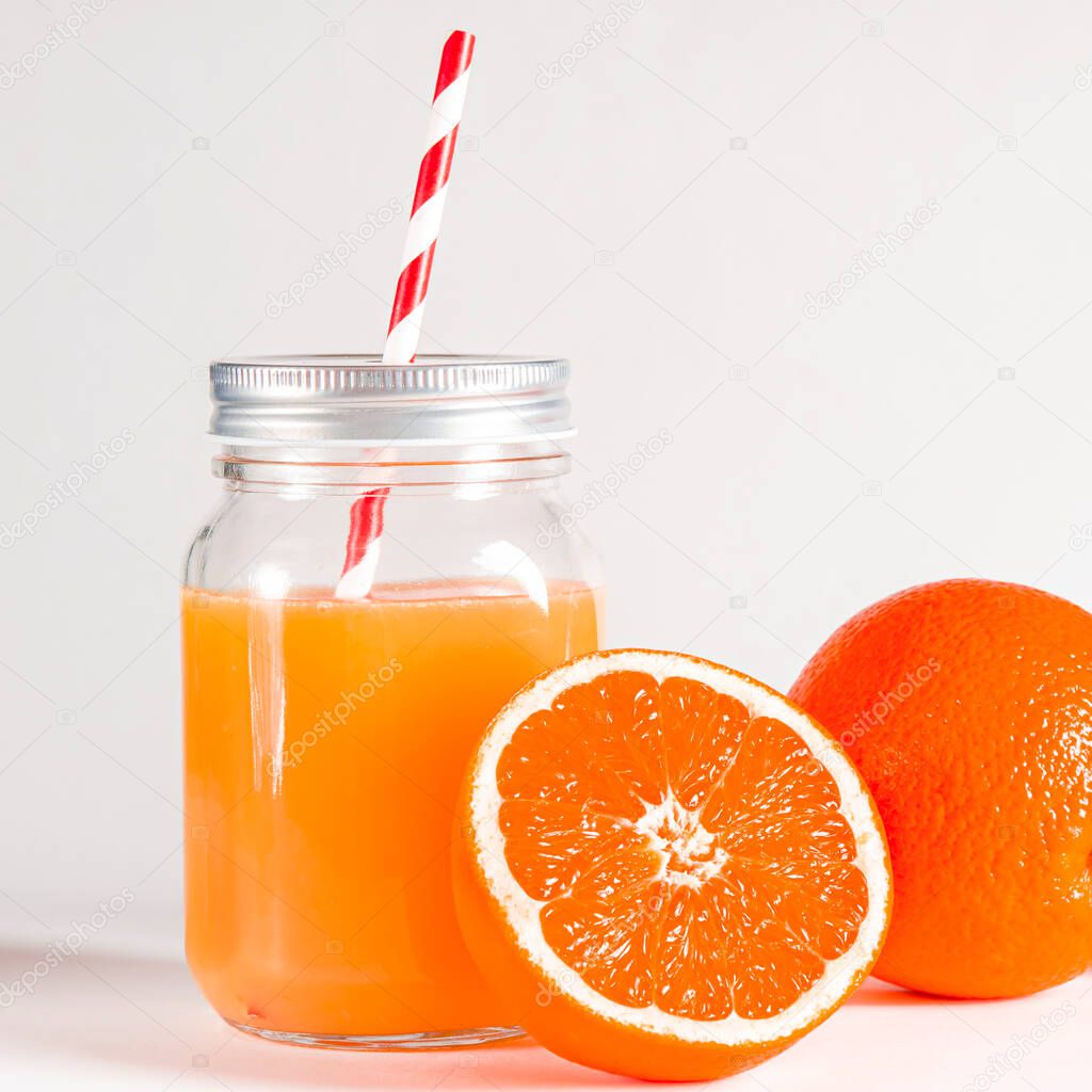 Glass jar with a tube with freshly squeezed orange juice stands on a white background next to fresh oranges. isolated