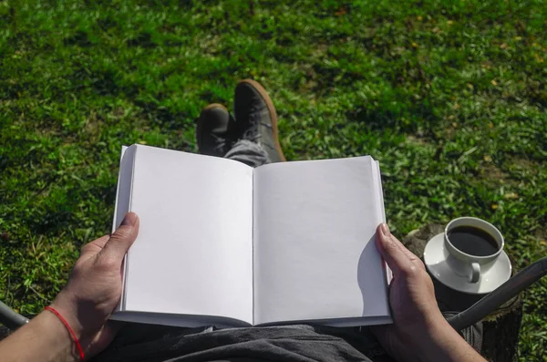 A mock-up of a white book in the hands of a man in the mouths of self-isolation in the garden. Close-up