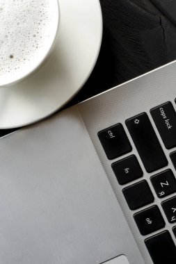 Serbest iş yeri. Bir dizüstü bilgisayar ve bir fincan köpüklü kahve siyah ahşap bir masada duruyor. Üst görünüm