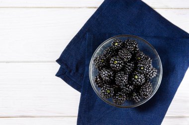 Meyveli böğürtlen beyaz ahşap bir masada cam bir tabakta yatıyor. Üst görünüm