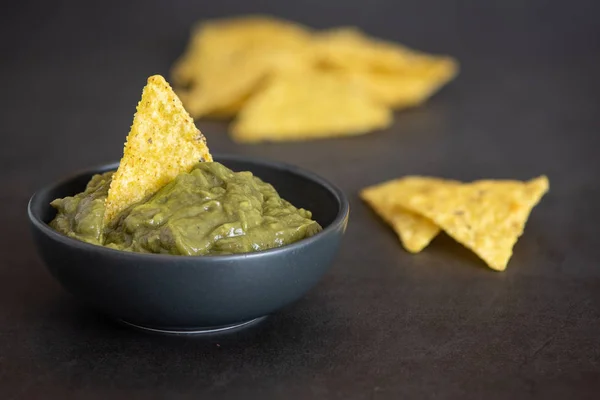 Grön Guacamole med nachos i skål på mörk bakgrund — Stockfoto