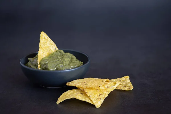 Grön Guacamole med nachos i skål på mörk bakgrund — Stockfoto