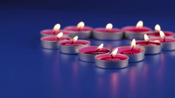 12本のピンクの香りのキャンドルが青い背景のテーブルの上で燃えます 彼らは小さな鉄キャンドルホルダーにあります 手前を中心に — ストック動画