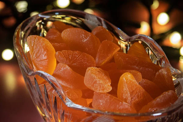 Portakallı marmelat dilimleri cam bir vazoda bir masanın üzerinde duruyor. Arka plandaki ışıklar yanıyor..