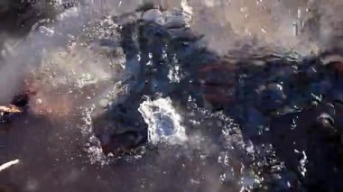 Gri buz arasında, güneş ışınları arasında bir kaynak akıntısı akar. Su mavi renkte..