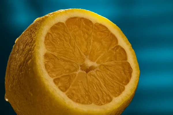 Mavi arka planda, taze limon bıçakla kesilir. Fetüsün kabuğu su damlalarıyla kaplı..