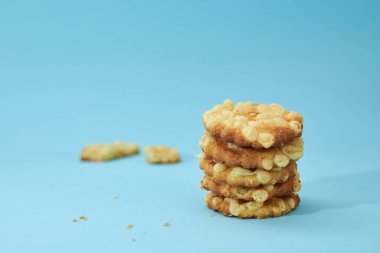 Peynirli kurabiyelerin solundaki kırık bisküviler, açık mavi arka planda izole edilmiş bir piramit gibi birbiri üzerine yerleştirilmiş. Besleyici atıştırmalıklar..