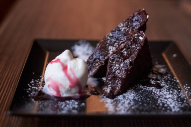 Bir parça çikolatalı kek ve siyah tabakta pembe soslu beyaz dondurma, ahşap masanın üzerinde duruyor. Lokantadaki lezzetli tatlıyı yakından çek.