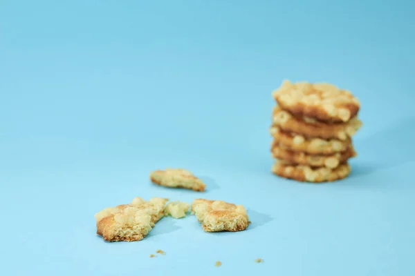 Pieces of broken biscuits on the left from cheese cookies, placed on top of each other, like a pyramid, isolated on light blue background. Nutritious snack.