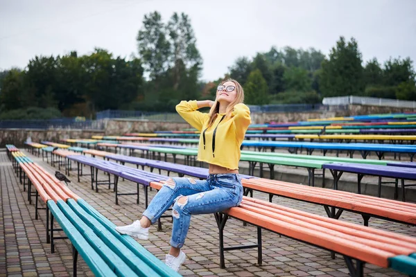 Jovem Loira Usando Capuz Amarelo Jeans Azuis Óculos Sentada Banco — Fotografia de Stock