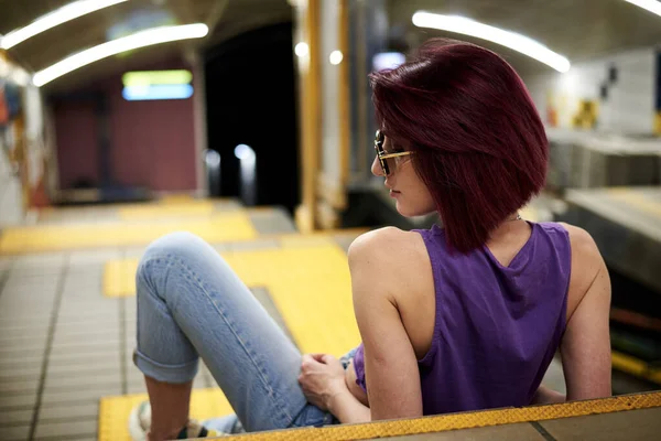 身穿紫色上衣 浅蓝色牛仔裤 戴着黑色太阳镜 留着勃艮第粉色栗色短发 坐在地铁站楼梯上的年轻女子 井下美女的富有创意的肖像 — 图库照片