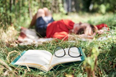Genç sarışın kadın, kırmızı gömlek ve siyah etek giyiyor, sırt üstü uzanıyor, kahverengi battaniyede uyuyor, bir sürü kitapla çevrili. Üniversite öğrencisi, okuduktan sonra yeşil çimlerde yorgun düşmüş. Kampüs eğlencesi.