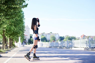 Uzun saçlı, paten giyen, sabah şehir parkında poz veren esmer bir kadın. Siyah bluz ve beyaz şort giyen kaykaycı portresi. Yaz etkinlikleri.