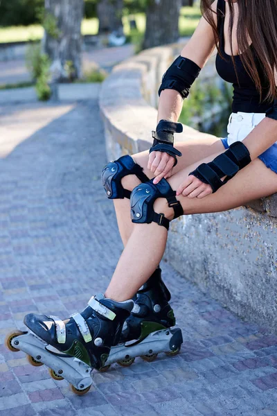 一张年轻女子的特写照片 她正在修理她的轮滑刀片膝盖安全设备 坐在长椅上 展示轮滑时穿着防护服的过程 — 图库照片
