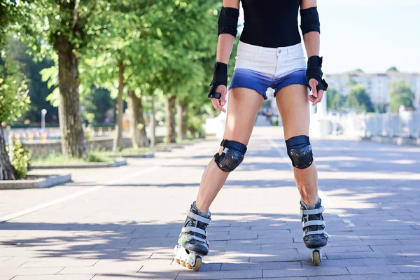年轻的女人 阳光灿烂的夏日早晨 带着绿树的滚翻公园 谭的腿 穿着轮滑鞋和防护用品 展示了进城的过程 — 图库照片