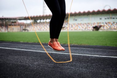 Spor kadınının bacaklarının yakın plan fotoğrafı, stadyumda ip atlarken. Genç bir kadın, siyah tayt giyiyor, yazın spor yapıyor. Sürecin içine atlama.