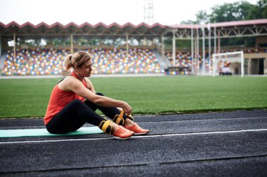 Kadının tam boy fotoğrafı, sarı bilek ağırlıkları giyme sürecini gösteriyor. Siyah tayt ve turuncu spor ayakkabı giyen genç bir kadın ağırlık antrenmanına hazırlanıyor..