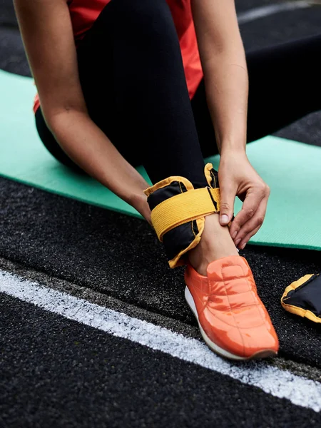 Close-up picture of woman\'s legs, showing process of putting on yellow ankle weights. Young woman, wearing black leggings and orange sneakers, is preparing herself for fitness training with weights.on