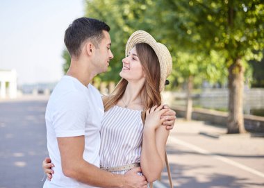 Beyaz tişörtlü, mavi şortlu yakışıklı esmer adam, açık saman şapkalı ve çizgili yaz mevsiminde güzel sarışın kadına sarılıyor. Genç çift birbirine aşık, sarılıyor, birbirlerine bakıyor, gülümsüyor..