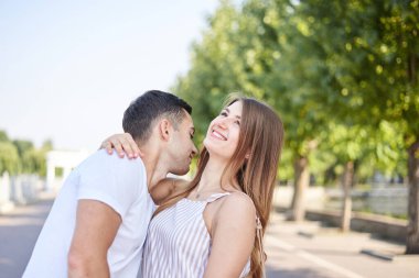 Beyaz tişörtlü, mavi şortlu yakışıklı adam yaz tatili boyunca güzel bir kadını öpüyor. Birbirini kucaklayan, birbirine bakan, gülümseyen genç bir çiftin yakın plan fotoğrafı..