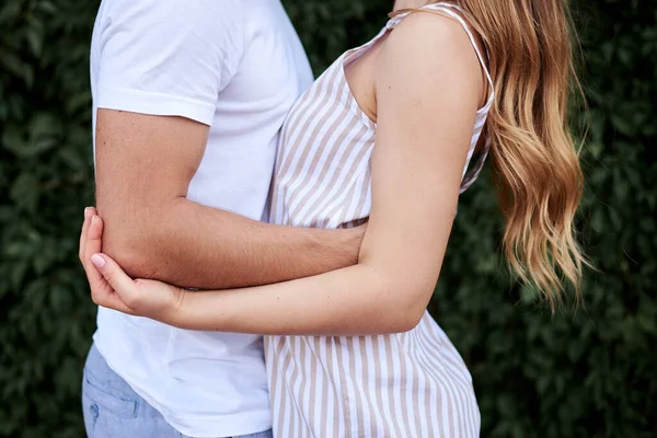 穿着白色T恤 蓝色短裤 拥抱女人在条纹夏天整体 恋爱中的年轻夫妇的身体 在绿叶墙附近 浪漫夫妻的亲密合影 — 图库照片