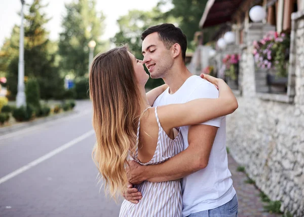 一对年轻夫妇在度假胜地的石墙边拥抱亲吻 漂亮的金发女人 总体上穿着条纹短发 在浪漫的约会中穿着白色T恤和蓝色短裤的黑发男人 — 图库照片
