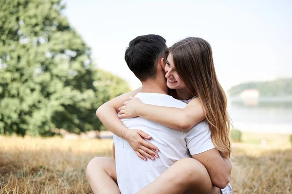 年轻夫妇坐在翠绿的黄草草坪上拥抱亲吻 在浪漫的约会中 金发女人总体上穿着条纹短裙 黑发男人穿着白色T恤蓝色短裤 — 图库照片