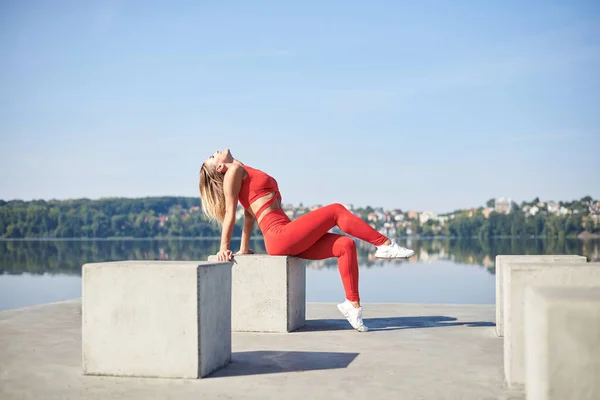 Mulher Loira Jovem Vestindo Roupa Fitness Vermelho Sentado Plataforma Concreto — Fotografia de Stock