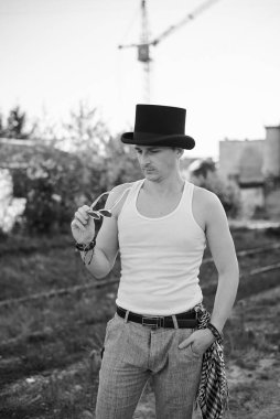 Beyaz bluzlu, siyah şapkalı, güneş gözlüğü takan ve düşünen bir gencin dörtte üçü. Terk edilmiş inşaat alanındaki yaratıcı adamın siyah beyaz fotoğrafı. Sanat Evi.