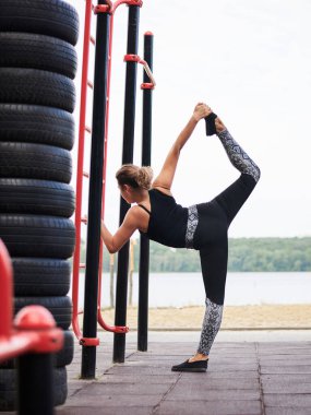 Siyah formalı, esmer bir kadın. Yaz aylarında İsveç Gölü 'nün yanındaki duvarda esneme egzersizleri yapıyor. Sporcu kadın dışarıda antrenman yapıyor. Sağlıklı enerjik yaşam tarzı kavramı.
