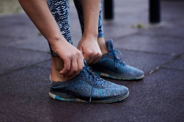 Genç sporcu kadın, gri tayt giyiyor spor ayakkabıları giyiyor. Hans 'ın yakın plan fotoğrafı spor ayakkabılarına ayakkabı bağcıklarını bağlama sürecini gösteriyor. Kadın, eğitime hazırlanıyor.,
