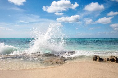 Açık mavi gökyüzü, turkuaz su ve beyaz bulutlarla Karayipler 'deki Rocky plaj manzarası. Kayalıklı güneşli sahil manzarası ve okyanusta kocaman köpüklü dalgalar. Panoramik tropikal manzara.