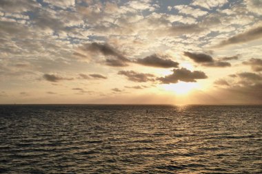Okyanusun ortasında nefes kesici bir gün batımı, sarı turuncu mavi gökyüzü ve beyaz bulutlar, yolcu gemisinin güvertesinden manzara. Tatil seyahati manzarası.