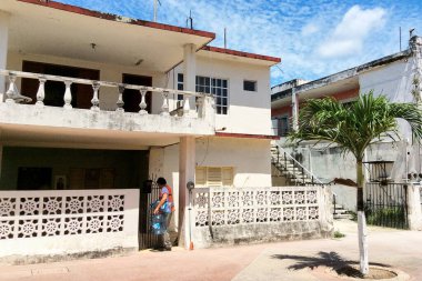 Cozumel / Mexico -22 Mar 2016: Meksikalı adam elinde büyük bir şişe suyla eski beyaz eve giriyor. Cozumel 'de renkli binaları olan parlak geleneksel cadde.