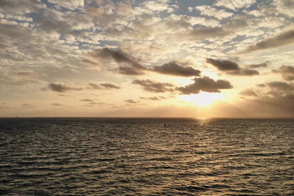 Okyanusun ortasında nefes kesici bir gün batımı, sarı turuncu mavi gökyüzü ve beyaz bulutlar, yolcu gemisinin güvertesinden manzara. Tatil seyahati manzarası.