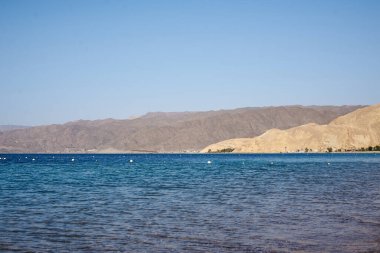 Arka planda sarı ve kahverengi kumlu kayalık dağlar olan güzel bir deniz manzarası. Tropik tatil köyü manzarası.