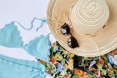 Beyaz arka planda izole edilmiş yaz tatili plaj aksesuarlarının düz bir resmi vardı. Nane mavisi mayo, güneş gözlüğü, renkli çiçekli atkı ve hasır şapka. Tropik tatil planı.