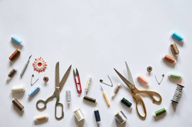 Beyaz arka planda izole edilmiş dikiş aksesuarlarının düz bir resmi vardı. Makas, renkli iplikler ve iğneler, el yapımı kullanıma hazır..