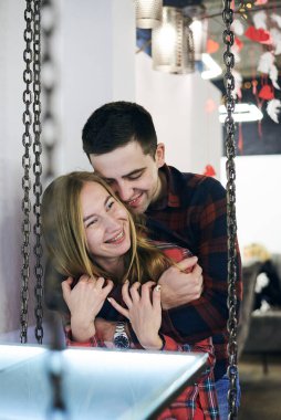 Aşık genç bir çift, kırmızı kareli gömlekler giyiyorlar, kahve dükkanında salıncakta oturuyorlar. Çekici adam kahve dükkanında güzel bir kadına sarılıyor. Romantik Sevgililer Günü Kutlaması